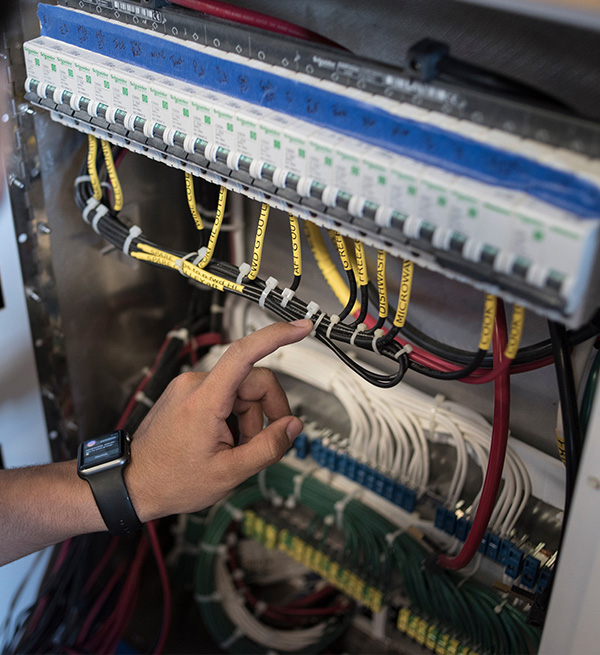 Electrical panel with labeled wires and a hand adjusting connections for marine systems.
