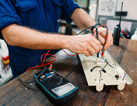 Technician testing electrical connections with a multimeter in a marine setting.